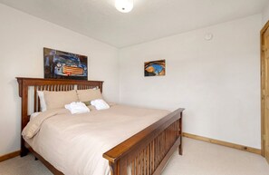 Une chambre à coucher avec un lit en bois, une literie de couleur beige et deux œuvres d’art accrochées au mur.