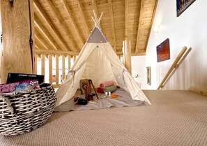 Une pièce avec un plafond en bois, une moquette blanche, une tente en forme de tipi et un panier contenant un livre.