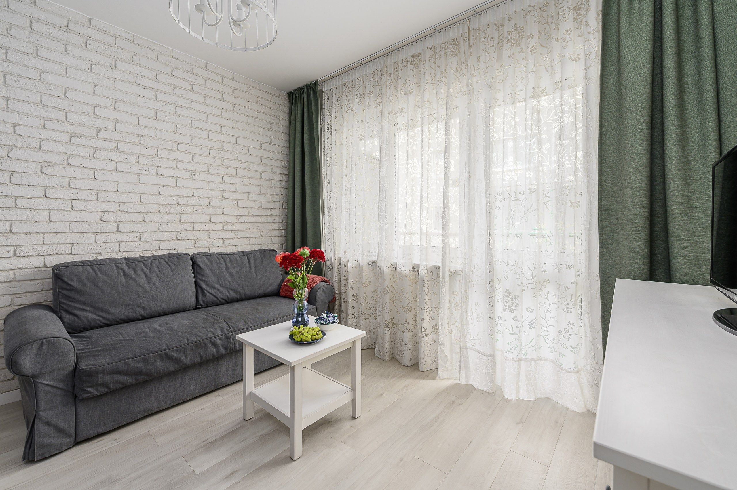Una sala de estar moderna con un sofá gris, una mesa de centro blanca con un jarrón de flores y un televisor sobre un mueble.