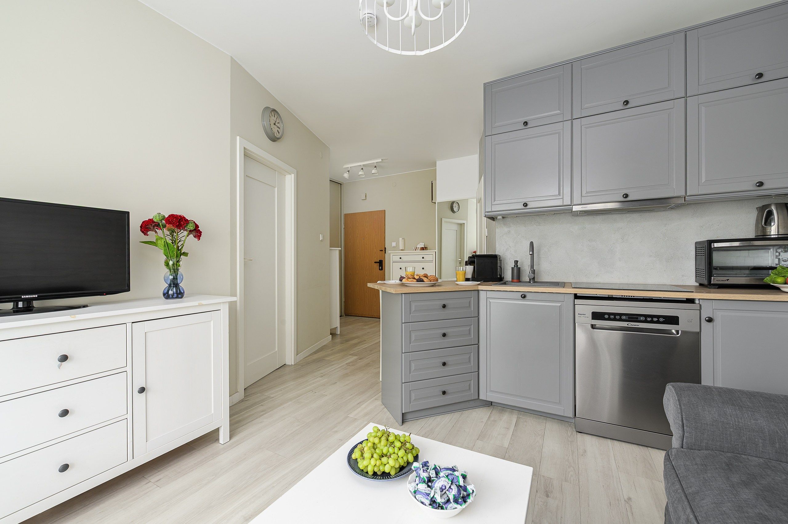 A modern kitchen with grey cabinets, a dishwasher, and a microwave. There is a dining area with a white table and a vase of flowers.