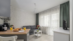 Una cocina moderna con pared de ladrillo blanco, una mesa de comedor con alimentos para el desayuno, un sofá y una ventana con cortinas translúcidas.