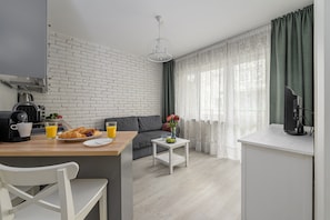A modern kitchen with a white brick wall, a dining table with breakfast items, a sofa, and a window with sheer curtains. - Wileńska P&O Apartments (Warszawa)