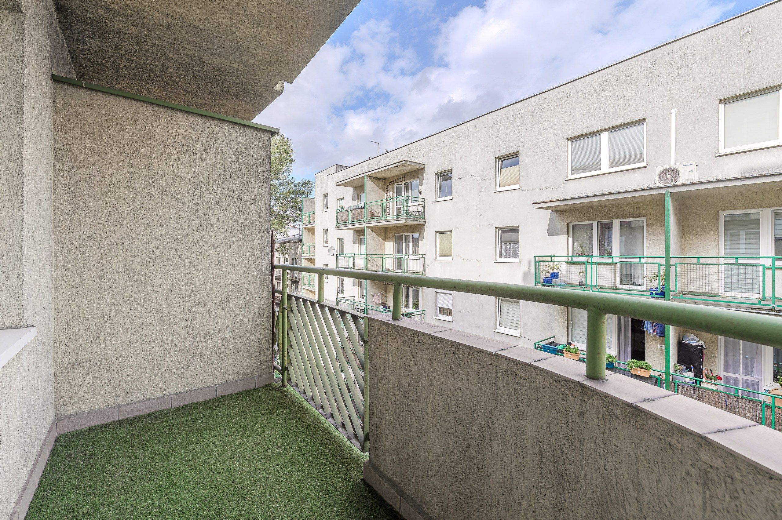 En balkon med kunstgræs, gelænder i metal og udsigt til nabobygninger.