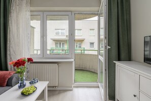 A room with a view of a building through a window, a radiator, a table with flowers and a bowl of fruit, and a television on a cabinet. - Wileńska P&O Apartments (Warszawa)