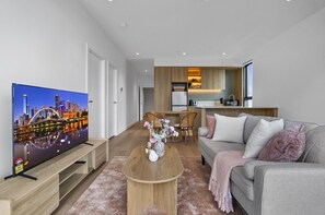 A modern living room with a flat-screen TV, a coffee table with flowers, a sofa with cushions, and a kitchen area in the background. - St Kilda Road 2-bed With Rooftop Access (Melbourne)