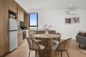 A modern kitchen with a dining area, featuring a round table with chairs, a view through a window, and a cityscape. - St Kilda Road 2-bed With Rooftop Access (Melbourne)