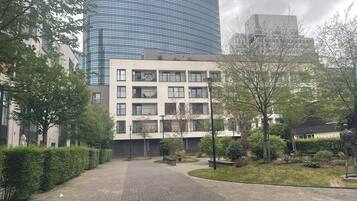 Een gebouw met een gebogen glazen gevel, een plat dak met meerdere ramen, en een geplaveid binnenhof met bomen en een standbeeld.