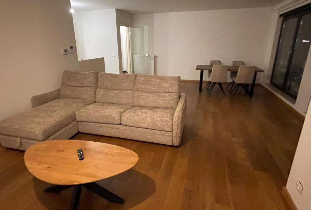 Een woonkamer met een hoekbank, een ronde salontafel en een eethoek met stoelen.