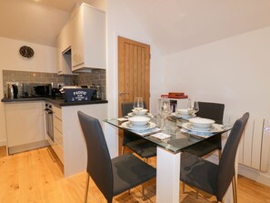 A compact kitchen with modern appliances, a dining area with a glass table and black chairs, and a wooden door. - Fishermans Loft (St Austell)