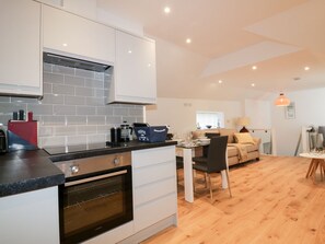 A modern kitchen with white cabinets, a built-in oven, and a dining area with a table and chairs. - Fishermans Loft (St Austell)
