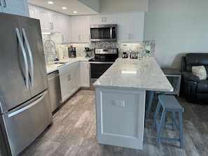 A modern kitchen with stainless steel appliances, a marble countertop, and a built-in island with stools. - Bay to Gulf Townhouse on Manasota Key (Englewood)