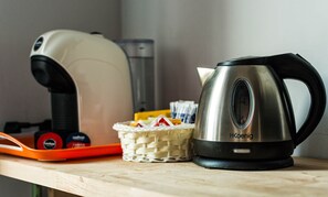 Ein Wasserkocher und eine Kaffeemaschine auf einer Holztischplatte, dazu eine Korb mit Teebeuteln und eine Teedose.
