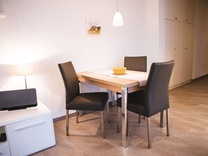 A dining area with a table, chairs, a lamp, and a television on a stand. - Holiday Apartment With 1 Bedroom (Zingst)