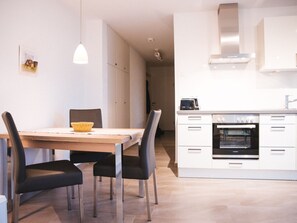 Une cuisine moderne avec des meubles blancs, un four encastré et un four à micro-ondes. On y trouve une table à manger avec des chaises et un luminaire suspendu.