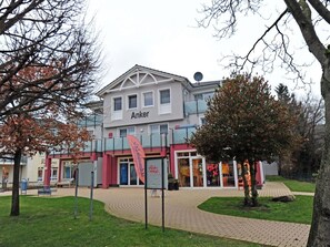 A building with the name 'Anker' on the facade, surrounded by a paved area with benches and trees. - Holiday Apartment With 1 Bedroom (Zingst)