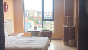 Habitación de hotel con cama, una mesita, una silla y vistas a edificios a través del ventanal.