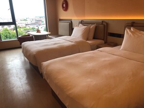 Quarto de hotel com duas camas, uma mesinha e vista da cidade através de amplas janelas.