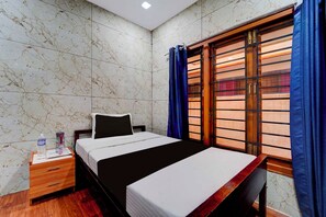 Una habitación de hotel con una cama, una mesita de noche, una botella de agua y un ventanal con cortinas.
