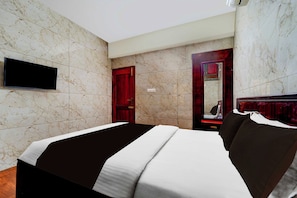 Habitación de hotel con una cama, televisión montada en la pared, una puerta de madera y un espejo.