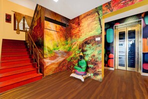 A staircase with red steps leading to a landing, a wall with a vibrant abstract mural, and a statue of a seated figure. - Townhouse Gandhipuram Central Bus Stand (Coimbatore)
