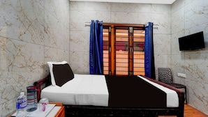 A hotel room with a bed, a TV, a window with curtains, a chair, and a table with a bottle and glasses. - Townhouse Gandhipuram Central Bus Stand (Coimbatore)