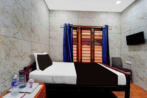 Habitación de hotel con cama, televisión, ventana con cortinas, una silla y una mesa con una botella y vasos.