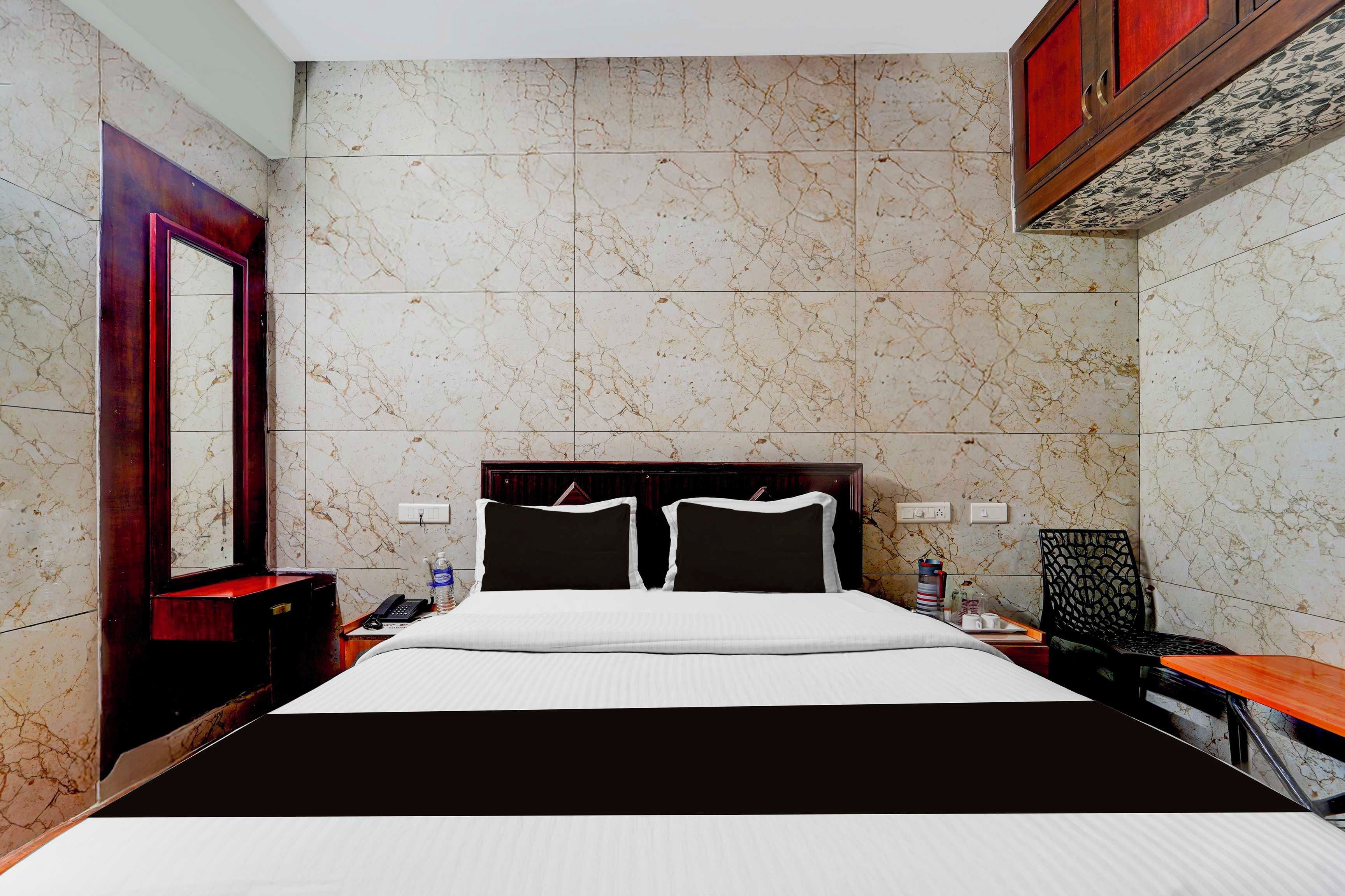 A hotel room with a marble-patterned wall, a large bed with black and white bedding, a wooden nightstand, a desk, and a chair.