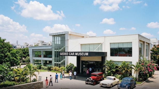 A modern building with a sign reading 'GEEDEE CAR MUSEUM' and a variety of classic cars parked in front. - Townhouse Gandhipuram Central Bus Stand (Coimbatore)