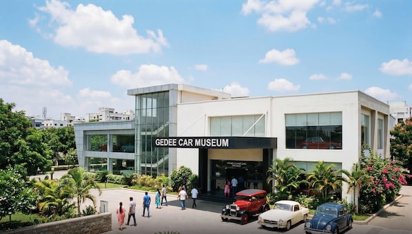 Un edificio moderno con un letrero que dice 'GEEDEE CAR MUSEUM' y varias autos clásicos estacionados al frente.