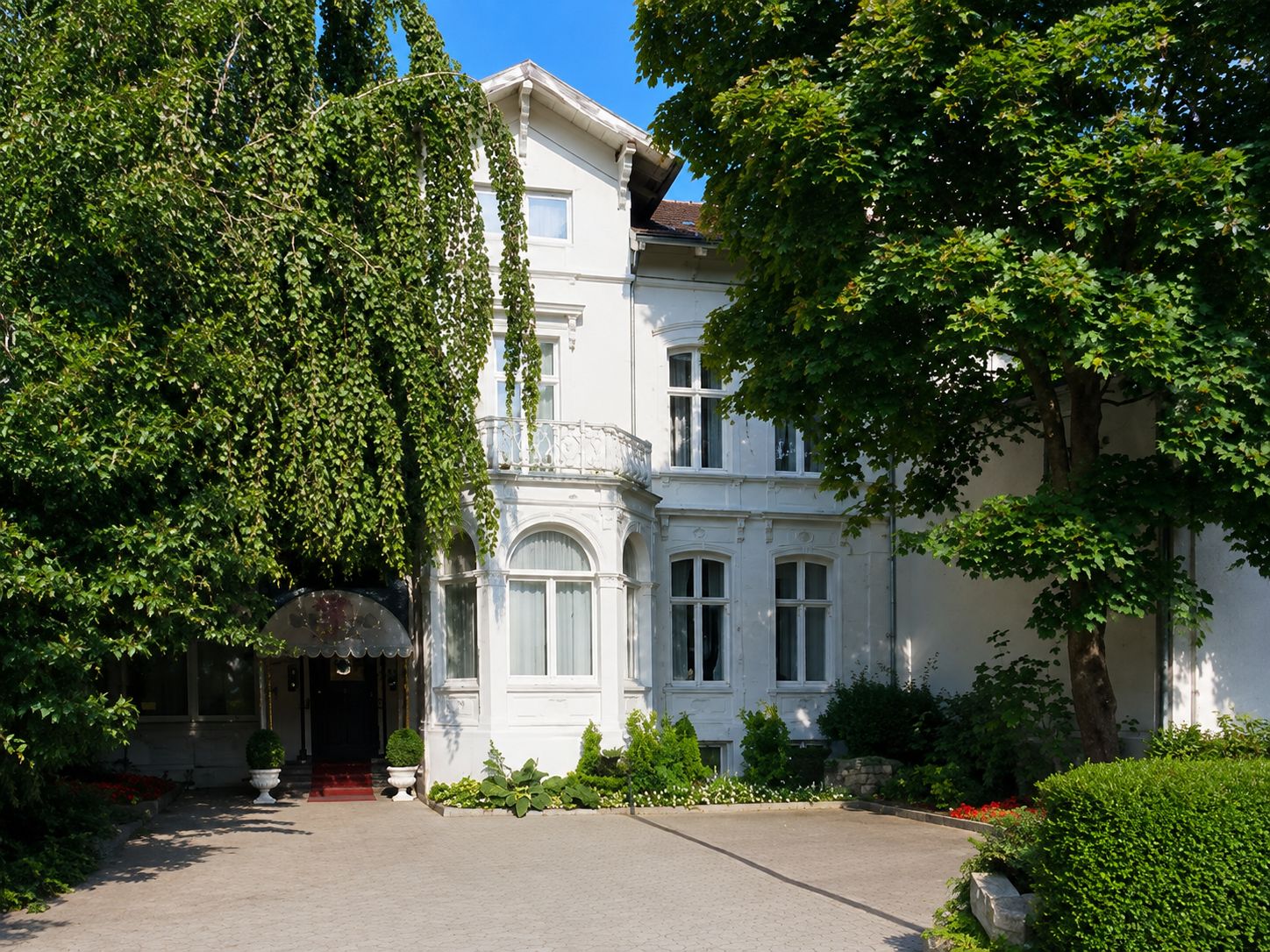 Un bâtiment blanc à la façade symétrique, doté de grandes fenêtres et d’une entrée centrale.
