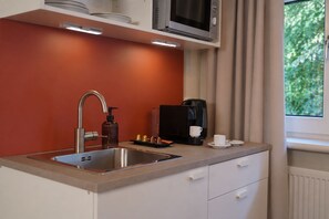A modern kitchen with a stainless steel sink, a coffee maker, and a microwave above it. - Studio Suite Hamburg (Hamburg)