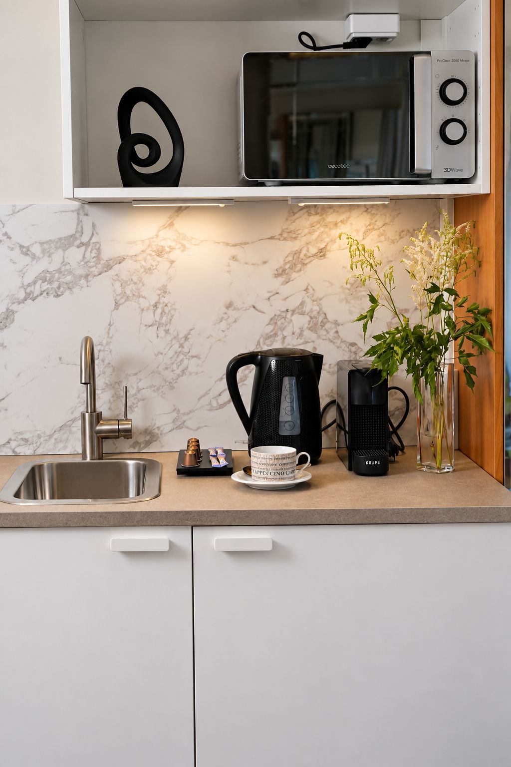 Une cuisine au design moderne, équipée d’un évier, d’une machine à café, d’un four à micro-ondes et d’un vase avec des fleurs.