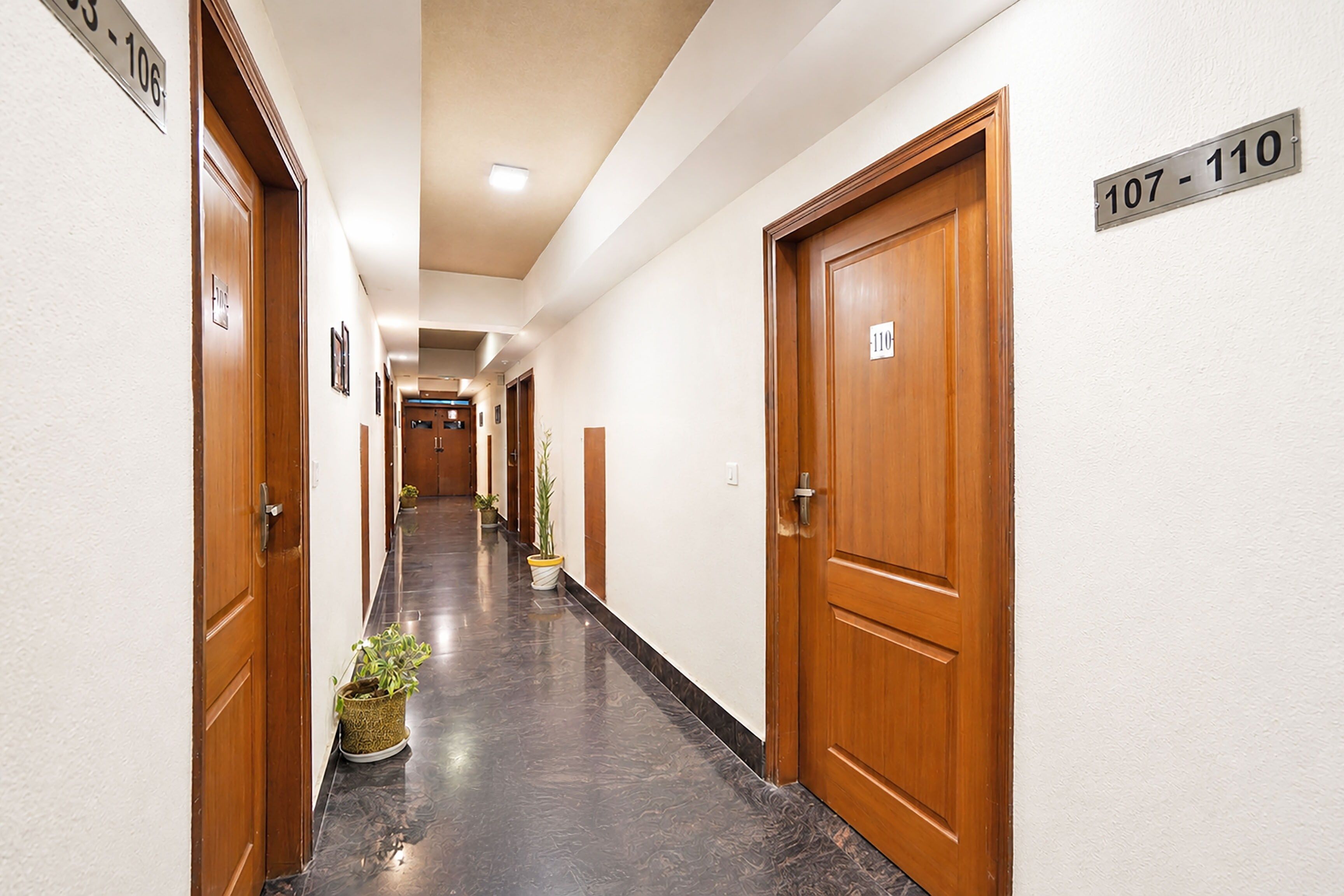 A hotel corridor with wooden doors, numbered room signs, and potted plants.