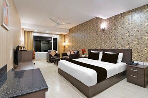 A hotel room with a bed, a desk, a chair, a sofa, a coffee table, a lamp, and a telephone.