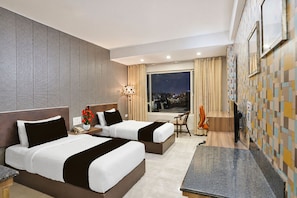 Une chambre d’hôtel avec deux lits, un bureau, une chaise, une télévision et une grande fenêtre donnant sur la ville.