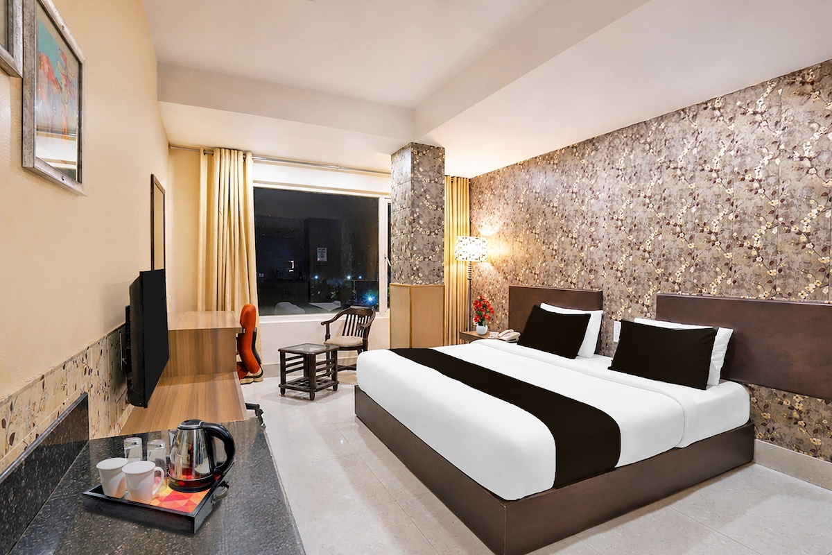 Une chambre d’hôtel avec un grand lit, un bureau avec une bouilloire, une chaise et une vue sur la ville la nuit.