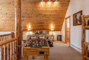 A cozy room with a wooden ceiling, a bed with patterned bedding, two lamps, and a foosball table. - Cozy Cabin Retreat with Hot Tub & Fire Pit for Summer in Island Park, Idaho (Island Park)