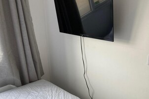 Una cama con colchón blanco y un televisor montado en la pared superior.