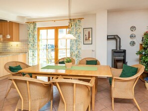 Un coin repas avec des chaises en osier, une table en bois, un luminaire suspendu et une vue sur l’extérieur grâce à une fenêtre agrémentée de rideaux.