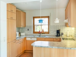A kitchen with wooden cabinets, a built-in dishwasher, a window with curtains, and a countertop with a coffee maker. - 10/t6 Holiday Home Park \"freesenbruch\" (Zingst)