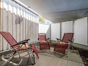 Un espace patio comprenant trois chaises pliantes et une table, une partie abritée et une clôture blanche.