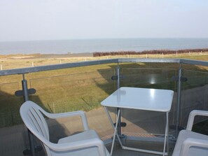 A balcony with a table and two chairs, overlooking a grassy area and the sea. - Holiday Apartment With 1 Bedroom (Cuxhaven)