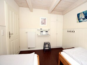 Ein Zimmer mit zwei Betten, einem Heizkörper, einem kleinen Hocker, einem Regal mit einem Drucker und einem Bild an der Wand.