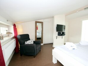 A hotel room with a bed, a chair, a television mounted on the wall, and a window with curtains. - Lapwing at Susanne-fischer-weg 31 (Wyk auf Foehr)