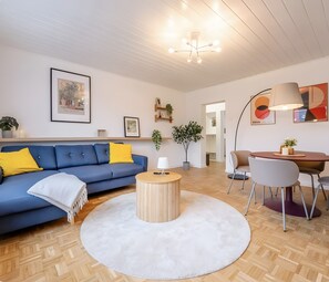 Ein modernes Wohnzimmer mit einem blauen Sofa, einem runden Couchtisch aus Holz und einem weißen Teppich.
