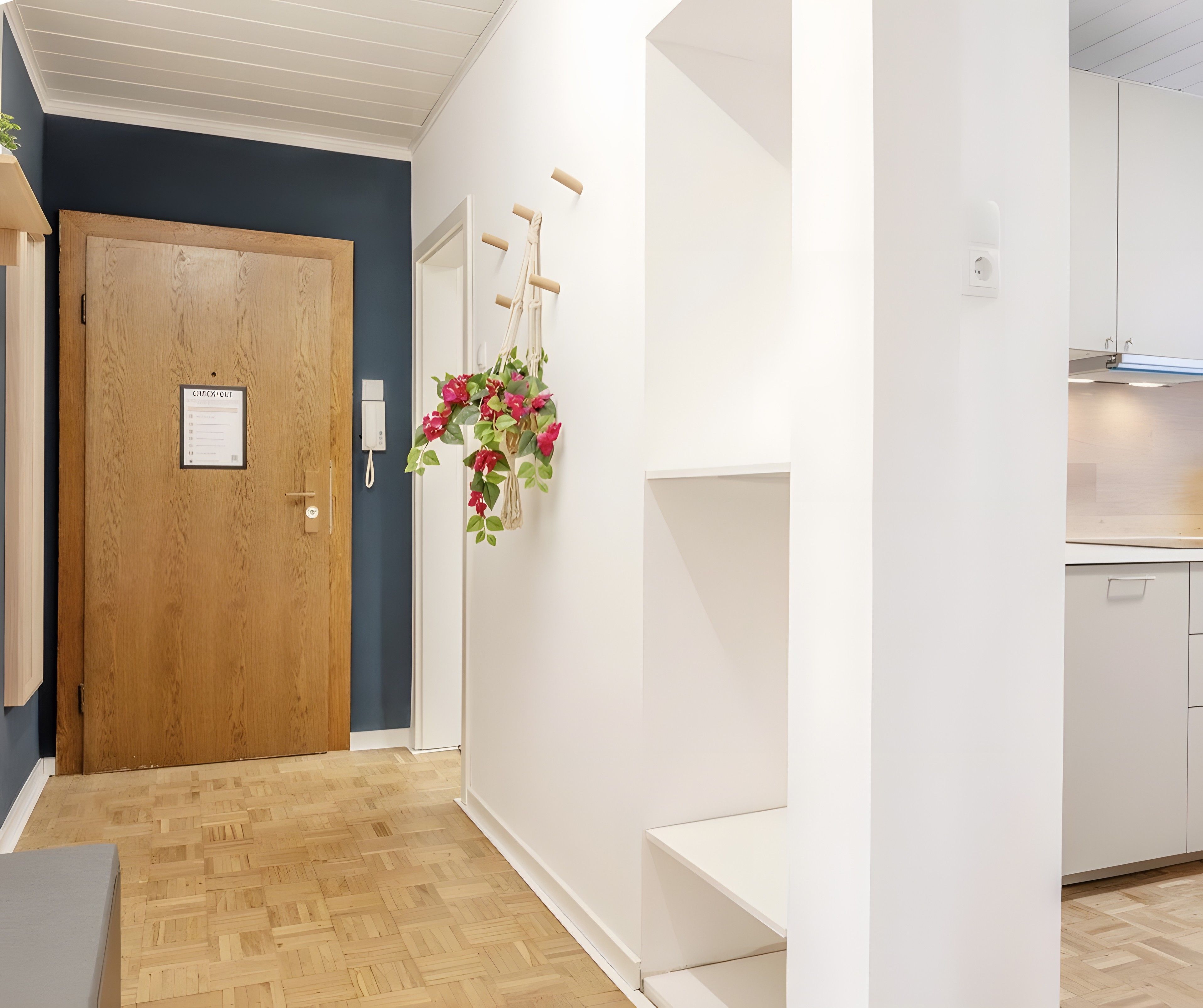 Ein Korridor mit einer Holztür, einem Check-out-Schild, einem an der Wand befestigten Telefon und einer blumengeschmückten Makramee-Wanddekoration.