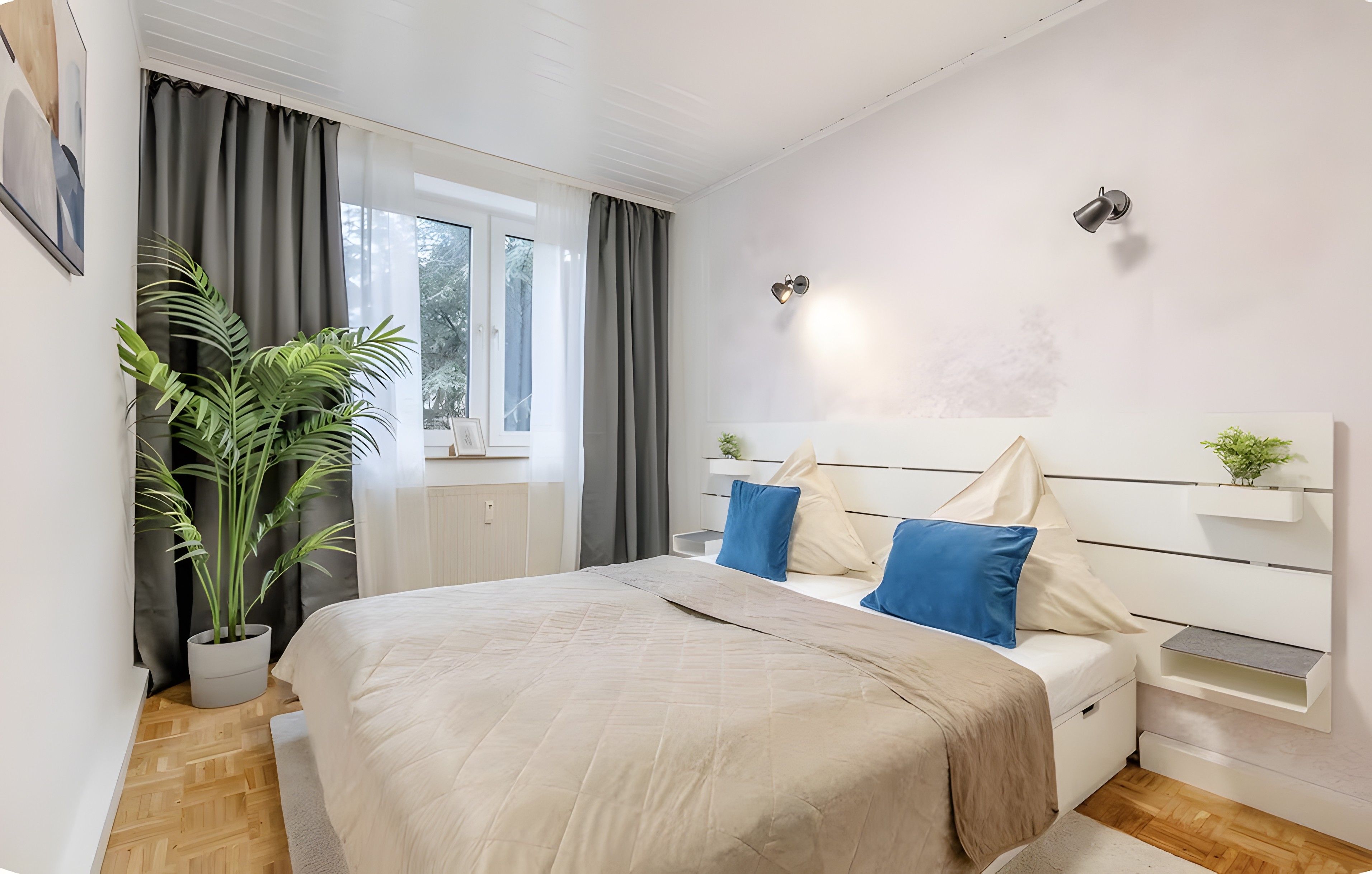 Un dormitorio moderno con cama, cortinas, una ventana, una planta y una lámpara de pared.