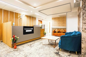 Un área de recepción con un mostrador de madera, un sillón azul, un sofá y una pequeña mesa con un jarrón de flores.