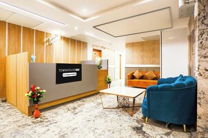 A reception area with a wooden reception desk, a blue armchair, a sofa, and a small table with a vase of flowers.