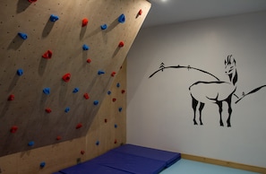 A climbing wall with various colored holds and a wall mural of a stylized animal.